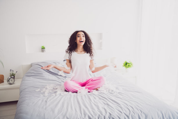 年轻迷人的女人全身照片坐在床上兴奋的羽毛穿着时尚的睡衣柔软舒适的卧室白色的房间里面图片下载