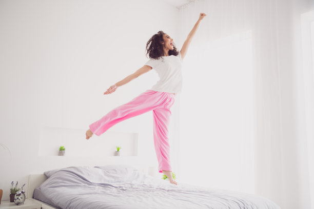 全身照片年轻迷人的女人跳飞超级英雄穿着时尚的睡衣柔软舒适的卧室白色房间内部图片下载