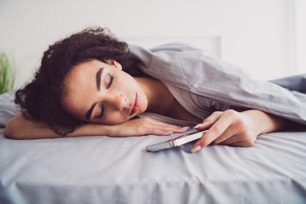 照片中迷人的年轻女子躺在床上，盖着毯子，装置睡觉，早上好，醒来家卧室的灯光白色的内部图片下载