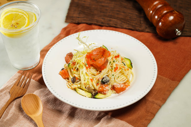 日式蟹黄烟熏三文鱼意面，配柠檬水，木勺和叉子装在盘子里，单独放在餐巾纸上，餐桌侧面的意大利食物图片下载