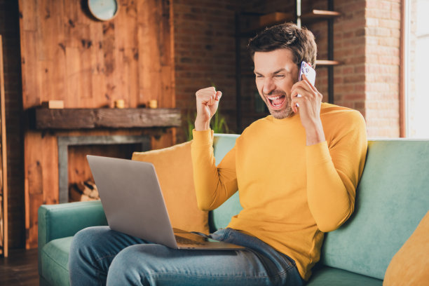 英俊成熟男人的照片肖像坐在沙发上网本获奖电话穿着黄色的衣服舒适的日光家室内客厅图片下载