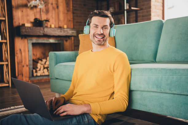 年轻人的照片肖像坐在地板上网本耳机穿着黄色的衣服花消遣宽敞的房子在室内房间图片下载