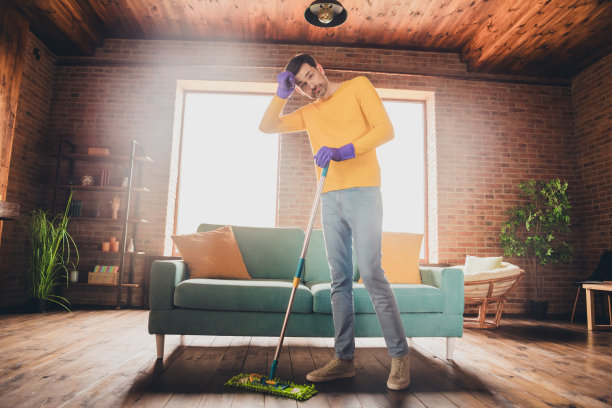 成熟男人的全尺寸照片拖地清洁房子疲倦困惑穿着黄色的衣服舒适的日光家室内客厅图片下载