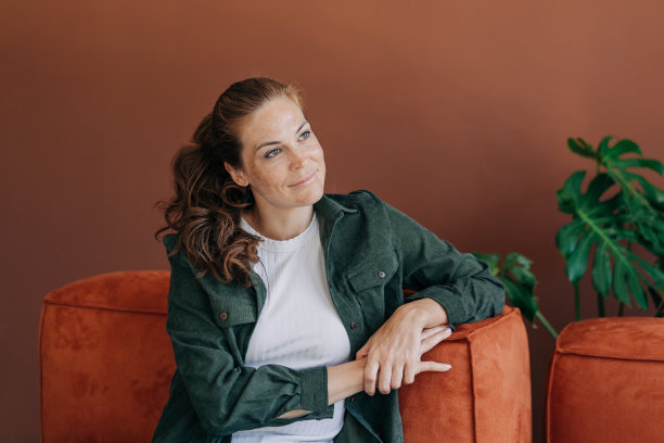 一位漂亮的年轻女子坐在沙发上若有所思地微笑着。图片下载