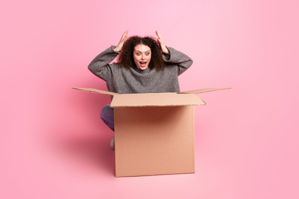 有吸引力的年轻女子的全尺寸照片偷看感兴趣的纸箱穿着时尚的灰色衣服孤立在粉红色的背景图片下载
