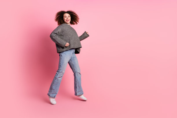 漂亮的年轻女孩的全身照片兴奋地跑步穿着时髦的灰色服装孤立在粉红色的背景图片下载