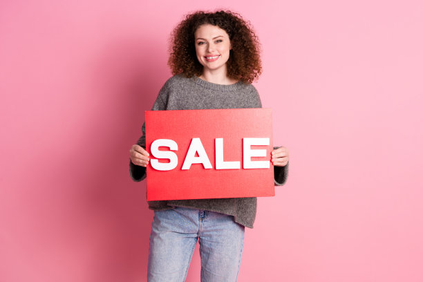 照片肖像可爱的年轻女士拿着销售板横幅穿着时尚的灰色服装孤立在粉红色的背景图片下载