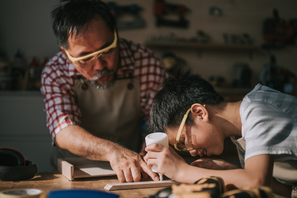 亚洲华人老木匠在木工车间教孙子木工图片下载