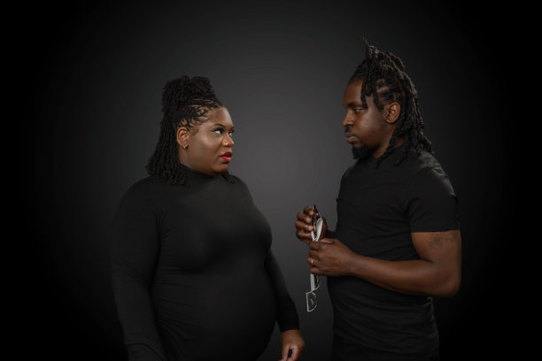 一对即将成为非裔美国人父母的夫妇在一间工作室里看着他们孩子的超声波照片，背景是深灰色的图片下载