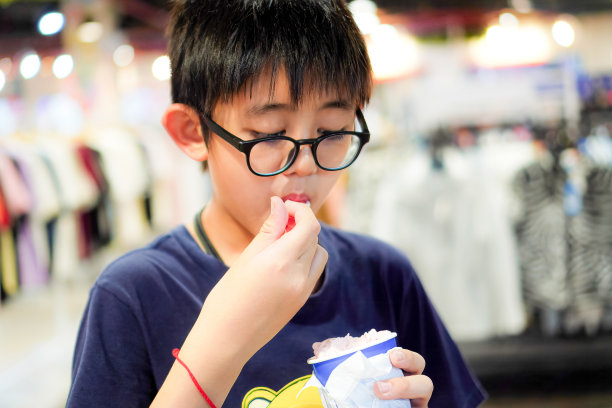 周日假期，泰国清迈，一个快乐的小男孩一边在购物中心散步，一边舀着冰淇淋。图片下载