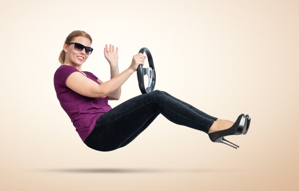 戴着墨镜的快乐微笑的年轻女子开着车，对着淡黄色背景的摄像机发出问候。汽车的概念图片下载