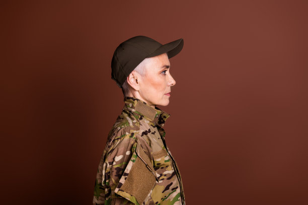 照片中自信严肃的退休妇女穿着迷彩服，看起来空旷孤立的棕色背景图片下载