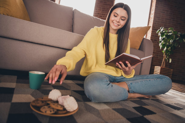 漂亮少女的全身照片坐在地板看书吃零食穿着黄色的衣服花消遣宽敞的房子在室内房间图片下载