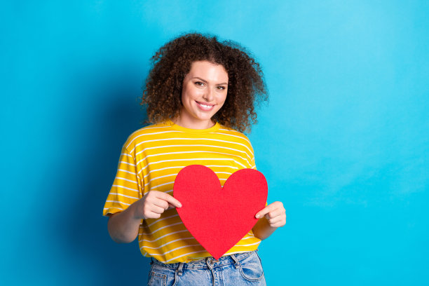 照片肖像迷人的年轻女子抱着心脏明信片穿着时尚的条纹黄色衣服孤立的蓝色背景图片下载