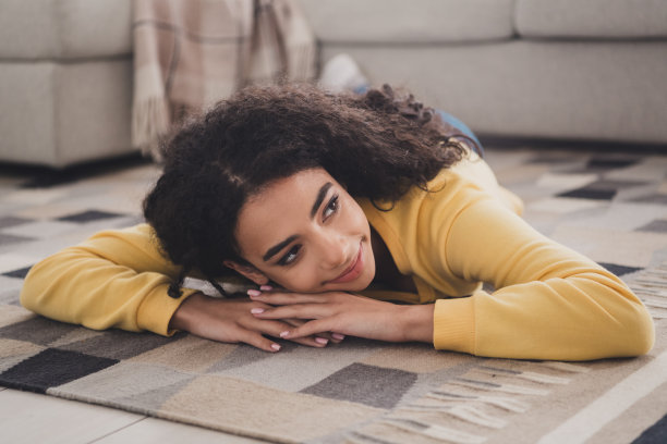 照片年轻的卷发滑稽可爱微笑的家庭女孩穿着黄色衬衫铺设地板格子地毯舒适的公寓室内图片下载
