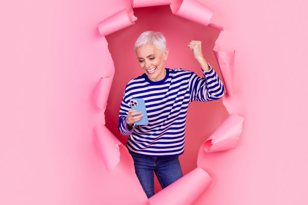 照片中可爱、开朗、高兴的女人穿着条纹时髦的衣服，在粉红色的背景上打破了纸墙图片下载