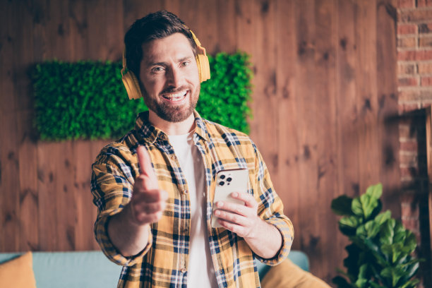 照片中的开朗积极的家伙穿着格子衬衫，听音乐，耳机，现代设备在室内的房子公寓房间图片下载