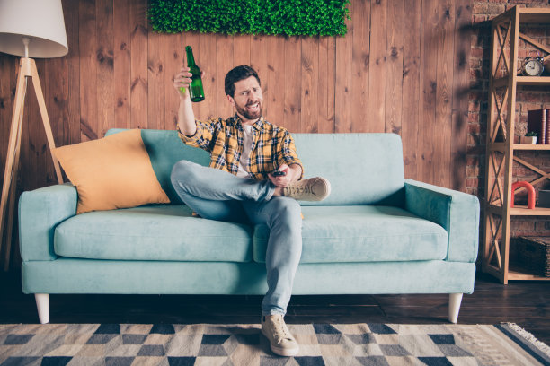 有吸引力的有趣的家伙穿着格子衬衫享受周末看比赛在房间里喝啤酒在家里的房子图片下载