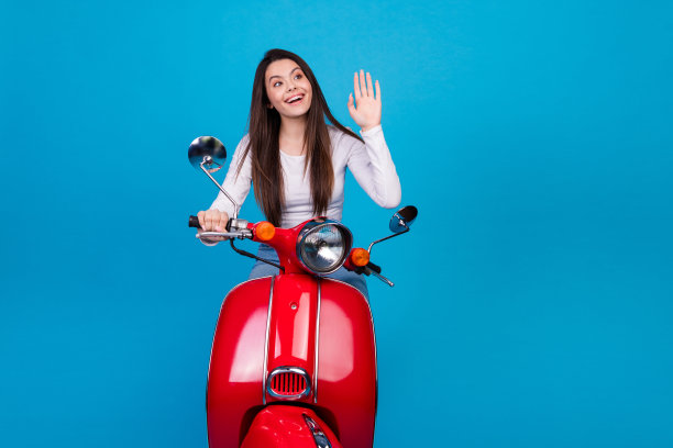 照片肖像迷人的少女兴奋地骑摩托车挥手hi穿着时尚的白色衣服孤立的蓝色背景图片下载