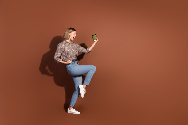 照片中疯狂快乐的女人穿着时髦的衣服喝咖啡成功空旷的空间孤立在棕色的背景上图片下载