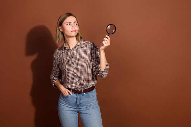 照片中可爱迷人的可爱女人穿着格子时尚的衣服，拿着放大镜，空旷的空间孤立在棕色的背景上图片下载