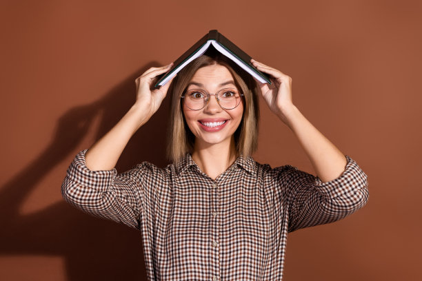 照片开朗可爱聪明的女人穿着格子时尚的衣服，手拿书孤立在棕色的背景图片下载