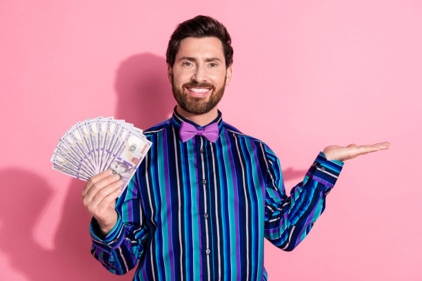照片有吸引力的积极的富人穿着时髦的衣服，手拿钱现金提供孤立的粉红色背景图片下载