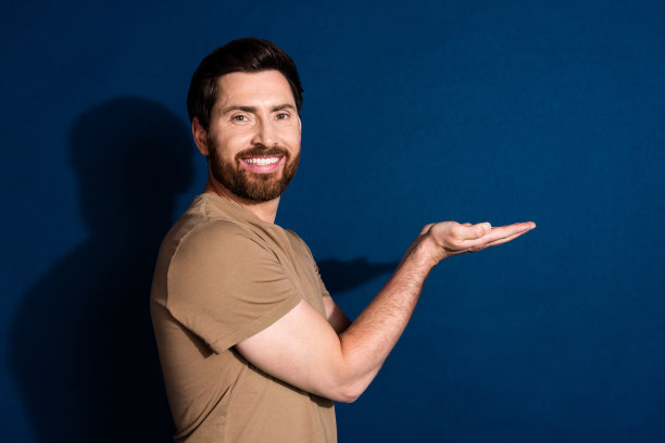 侧面侧面照片英俊的男子有胡子穿着米色t恤手掌握对象空空间孤立在深蓝色的背景图片下载