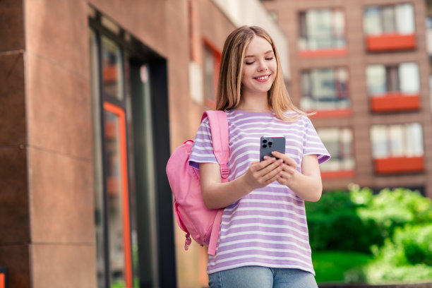 照片中，漂亮开朗的女士穿着紫色t恤，背着传达现代设备的背包，在城市街道上享受户外散步图片下载