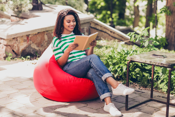 漂亮的年轻女子的照片，坐在袋子里看书，闲暇时间，周末，户外公园，新鲜空气图片下载