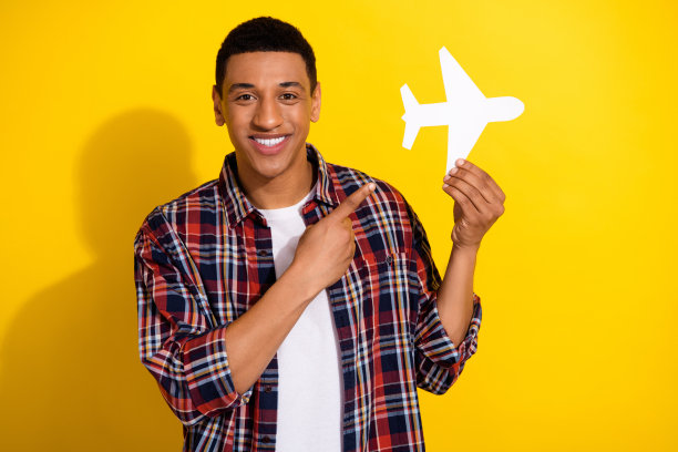 照片上，一个积极向上的男人，留着时髦的发型，穿着格子衬衫，手臂上有白色的纸飞机，孤立在黄色的背景上图片下载