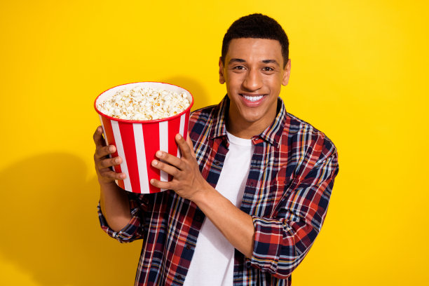 一个开朗的好男人，穿着时髦的格子衣服，看电影，在黄色的背景上看美味的爆米花图片下载