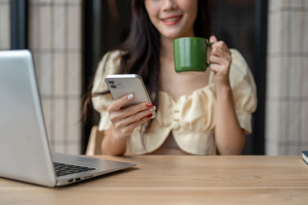 一张裁剪过的照片显示，一位女士在室内的一张桌子上一边喝咖啡一边查看手机信息。图片下载