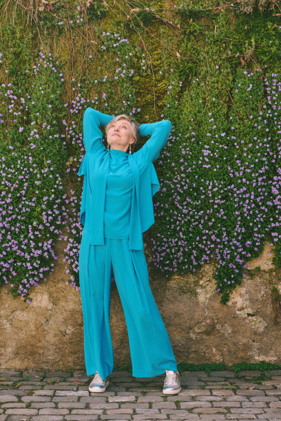 户外时尚的全身画像55 - 60岁的妇女摆姿势旁边紫色的花朵，穿着蓝色的一套衣服图片下载