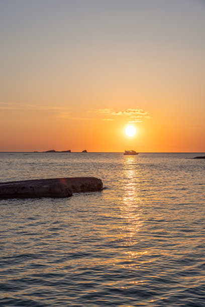西班牙伊比沙岛卡拉孔塔日落的垂直照片，在地平线上有一艘游船。夕阳把温暖的光辉洒在海面上图片下载