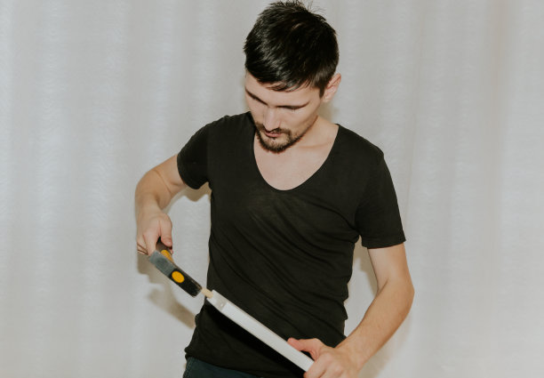 一个年轻人把一根木钉子钉进双层床的一个洞里。图片下载