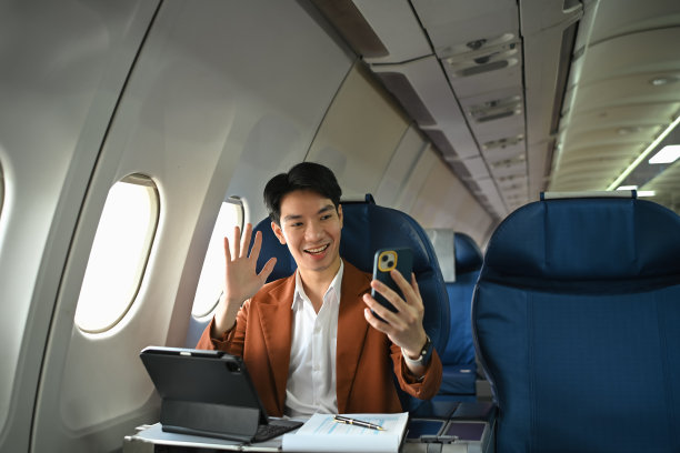 愉快的亚洲商务人士坐在机舱里用智能手机打视频电话或自拍图片下载