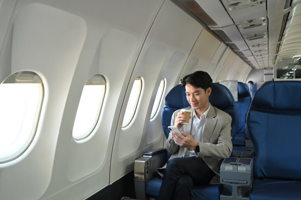 千禧一代的商人在飞机上一边喝咖啡一边玩手机图片下载