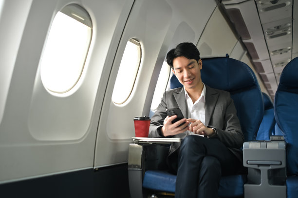 成功的亚洲商人在飞机上穿着西装，坐在靠窗的位置使用智能手机图片下载