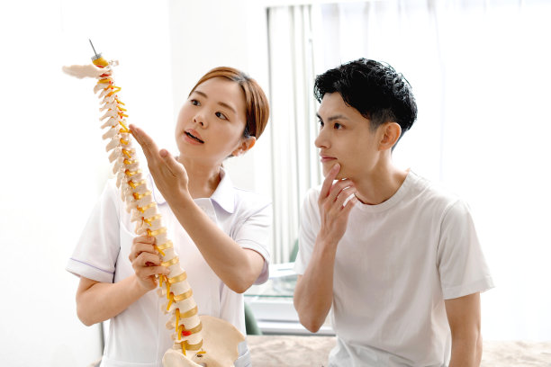 一名身穿白大褂的女医务工作者(指压师)正在用脊椎模型向一名男病人解释。图片下载