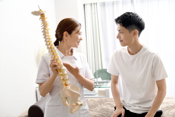 一名身穿白大褂的女医务工作者(指压师)正在用脊椎模型向一名男病人解释。图片下载