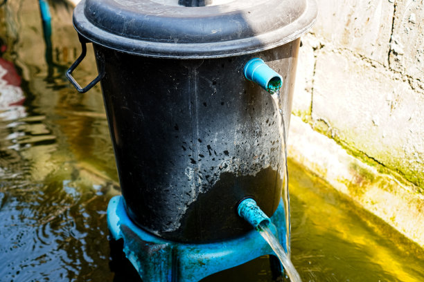 一个锦鲤池滤水系统的图片，由简单的回收材料制成，如旧水箱和水管，根据家庭可持续发展概念的原则。图片下载