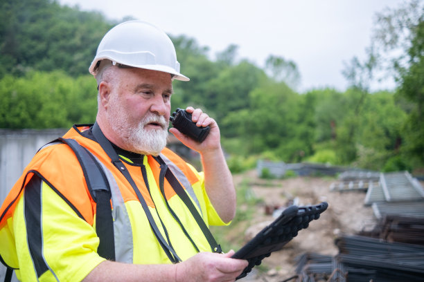 一大清早，戴着白头盔、白胡子、穿着反光背心、手提电脑包的工程师在大桥施工现场。图片下载