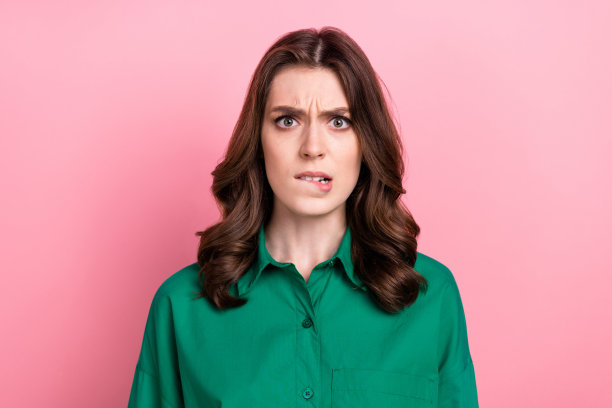 照片不确定怀疑的女人穿绿色衬衫咬嘴唇孤立的粉红色背景图片下载