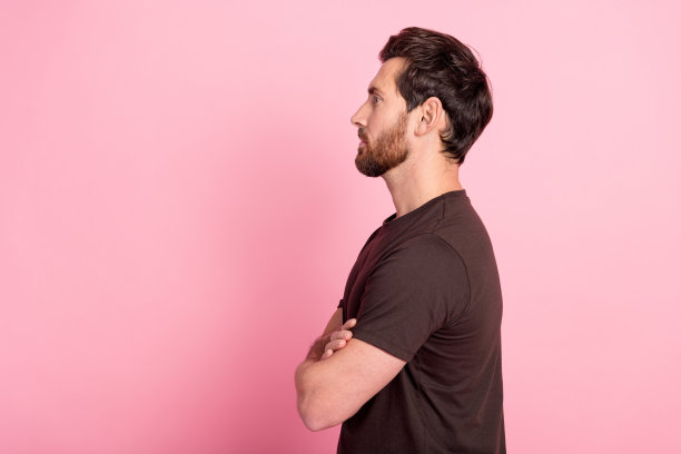 侧面侧面照片严肃的男人鬃毛穿着棕色t恤手臂折叠看起来空白空间孤立在粉红色的背景图片下载
