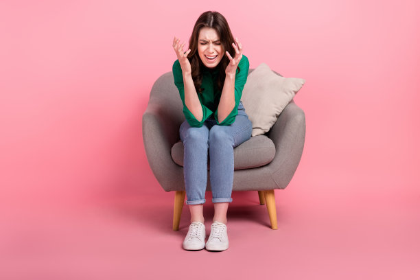 全身照片的沮丧哭泣的女人穿着绿色衬衫坐在沙发上大喊孤立的粉红色背景图片下载