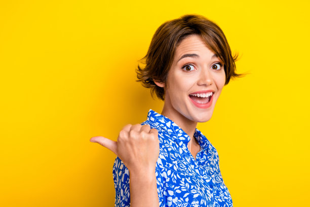 照片的闪亮印象的年轻女士穿着印花衬衫显示拇指背面空白空间孤立的黄色背景图片下载