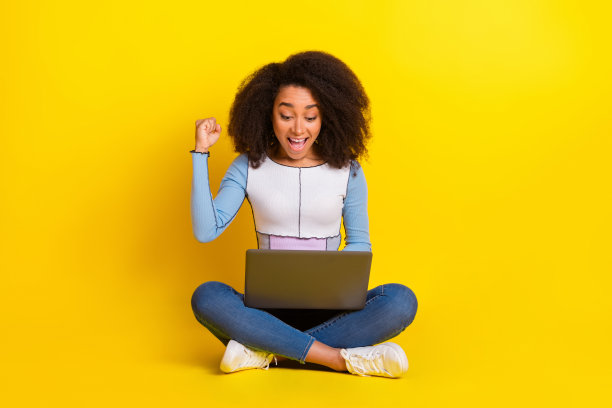 漂亮的年轻女孩的全尺寸照片坐在地板上网本获胜穿时髦的蓝色服装孤立的黄色背景图片下载