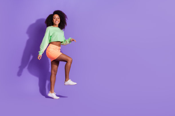 年轻的美国女孩的全身长度的照片，波浪卷曲的头发雪佛兰穿迷你裙和顶部台阶孤立的紫罗兰色背景图片下载