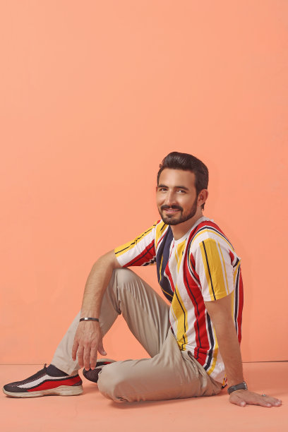 一个年轻的时尚男子的肖像，橙色背景，条纹t恤全高，坐着微笑的照片图片下载